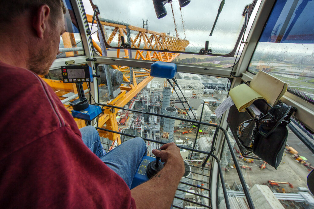 A tower crane operator keeps his eyes on the load and ears on the signal man.