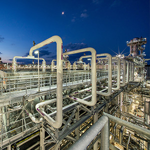 Racks de tuberías en una instalación de gas natural licuado iluminados bajo un cielo nocturno azul oscuro