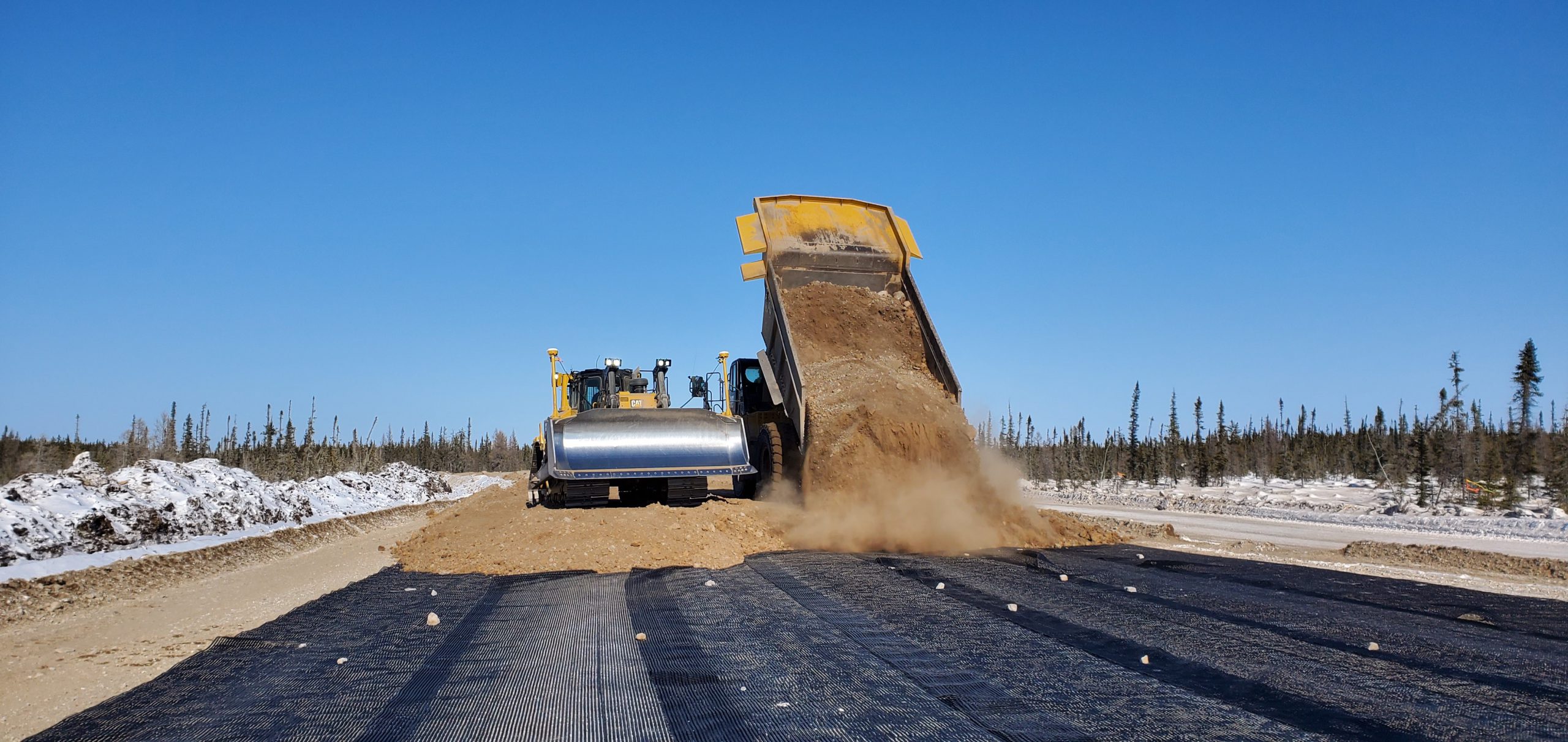 Crews add a layer of geogrid to reinforce the soil under the gravel top. 