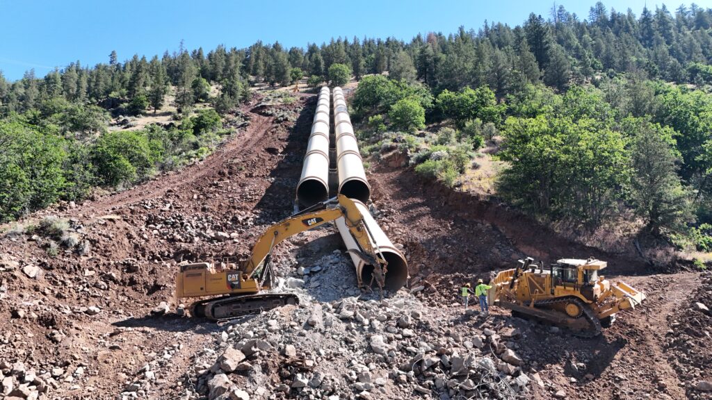 One of the most challenging aspects of demolishing the JC Boyle earthen dam in Oregon was the removal of double penstocks, each about 10 feet in diameter. Water was kept level for about two miles, then dropped down the steep mountain in penstocks to drive power. The team brought in track line excavators to repel equipment down the steep slopes.