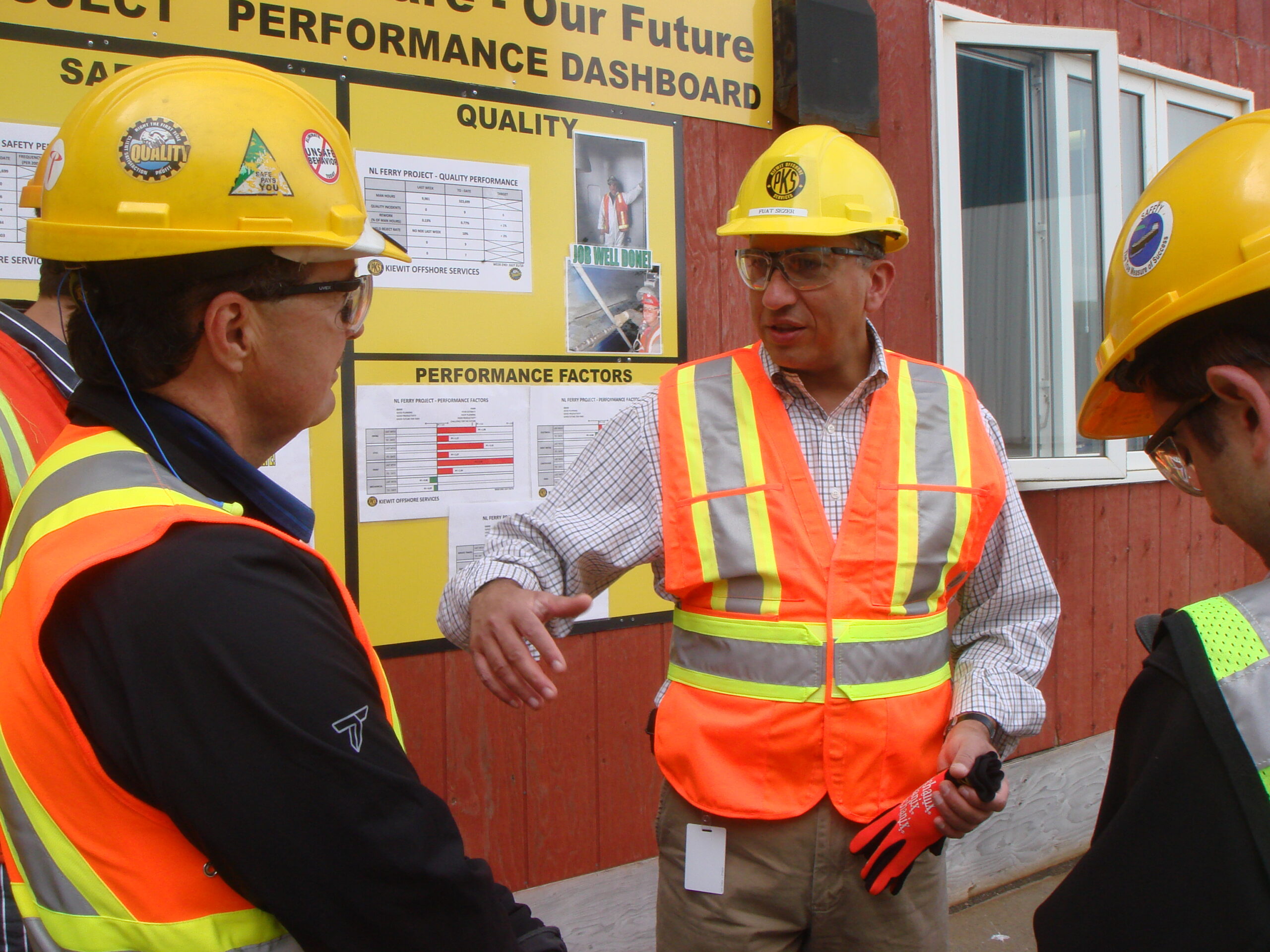 Crews gather around Sezer as he walks through safety and quality metrics posted on a continuous improvement dashboard with the slogan “Our Yard. Our Welfare. Our Future.” 