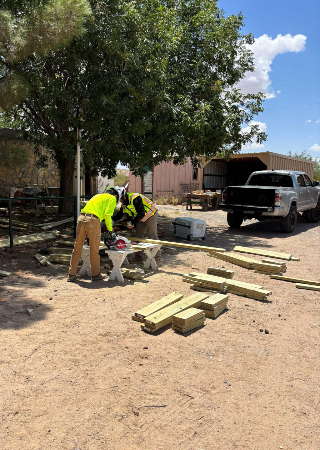 Two interns in safety vests and hard hats saw a piece of wood.